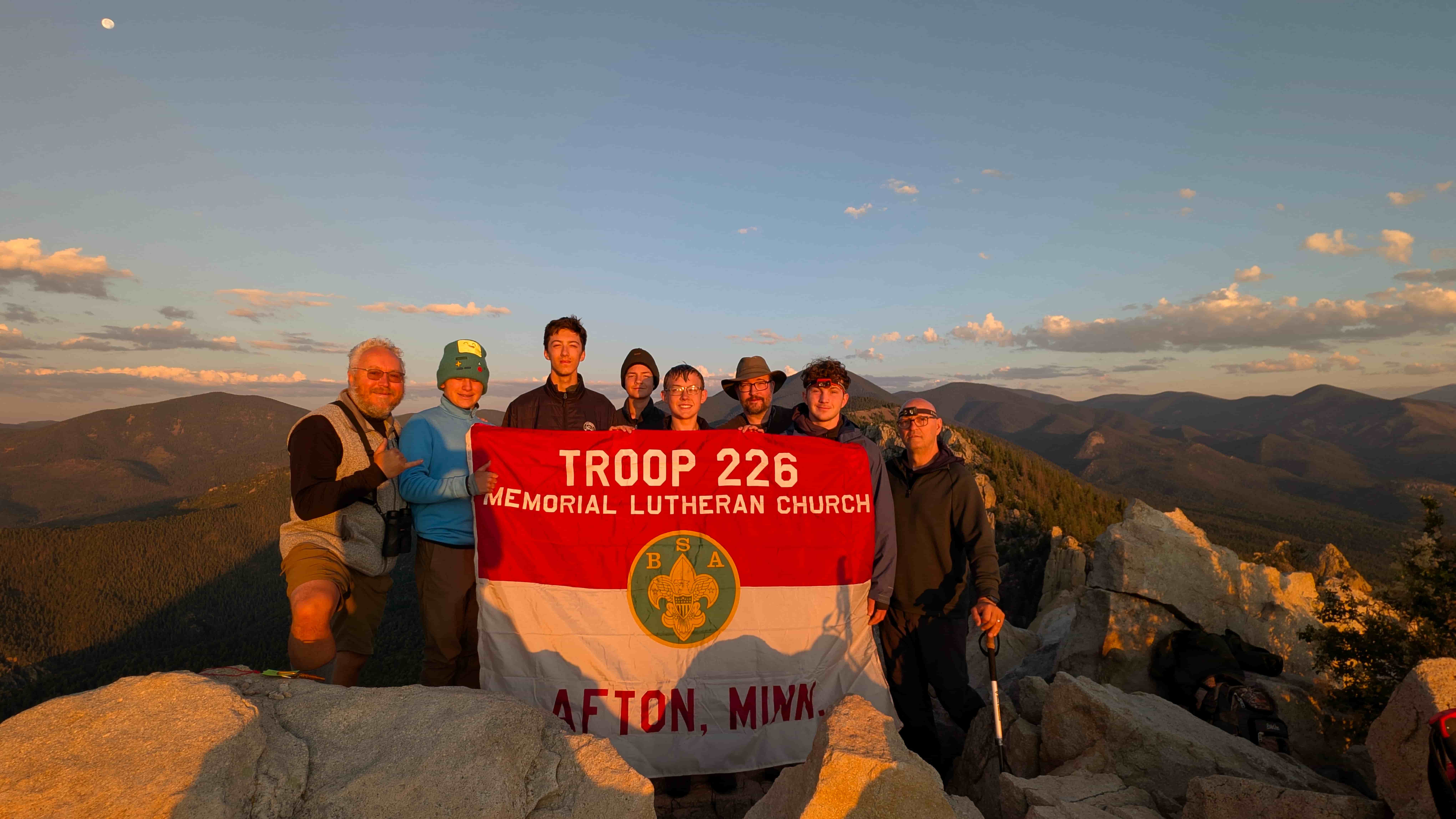 Troop 226 holding their banner at the mountain summit at golden hour